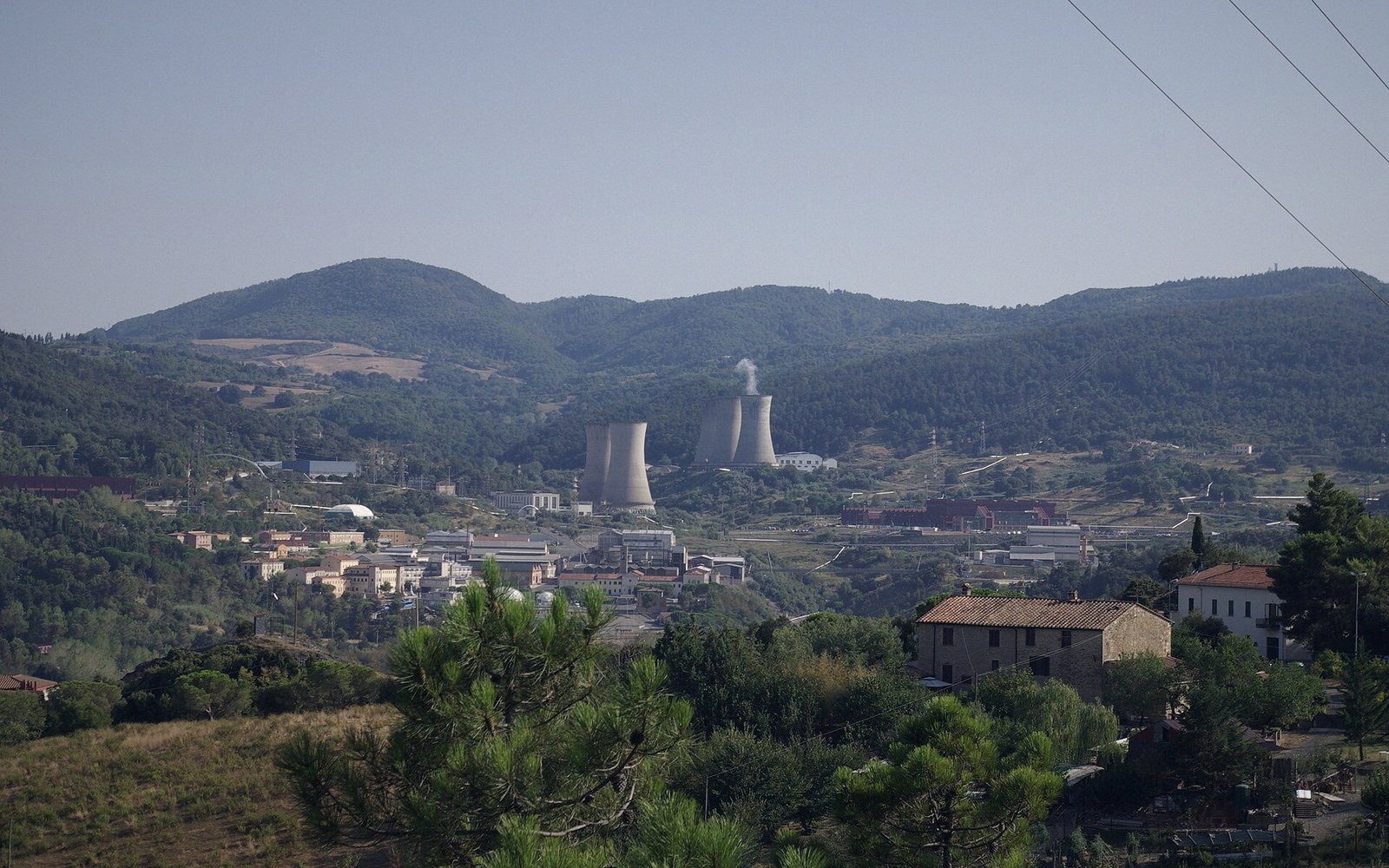 A geothermal wellhead venting steam on a Tuscan hillside