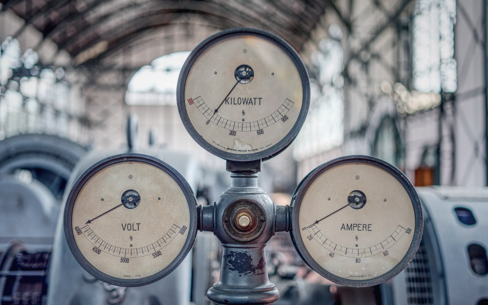 Three vintage gauges labeled kilowatt, volt and ampere mounted in an industrial hall