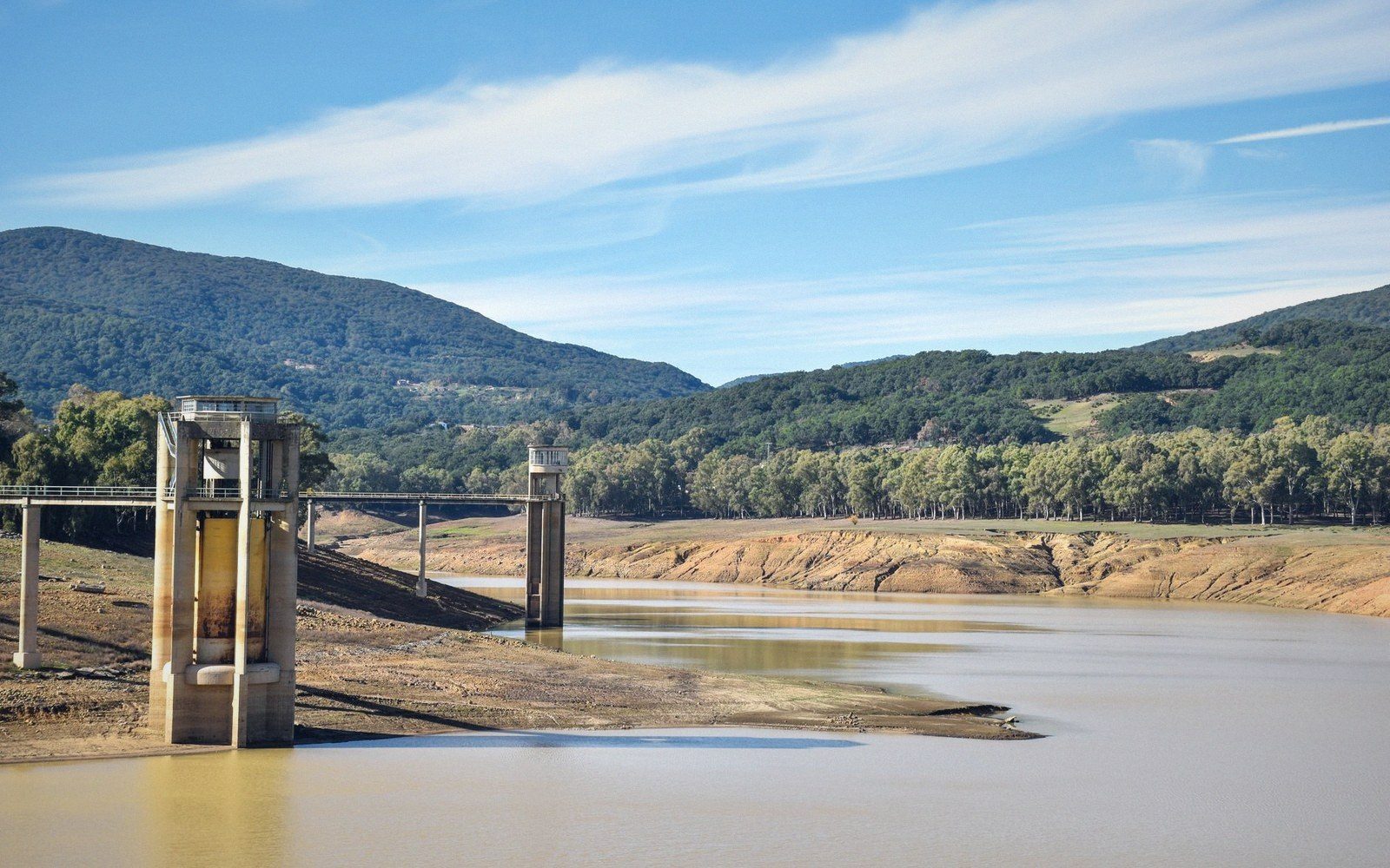 Concrete water intake towers stand in a reservoir with a low, exposed shoreline