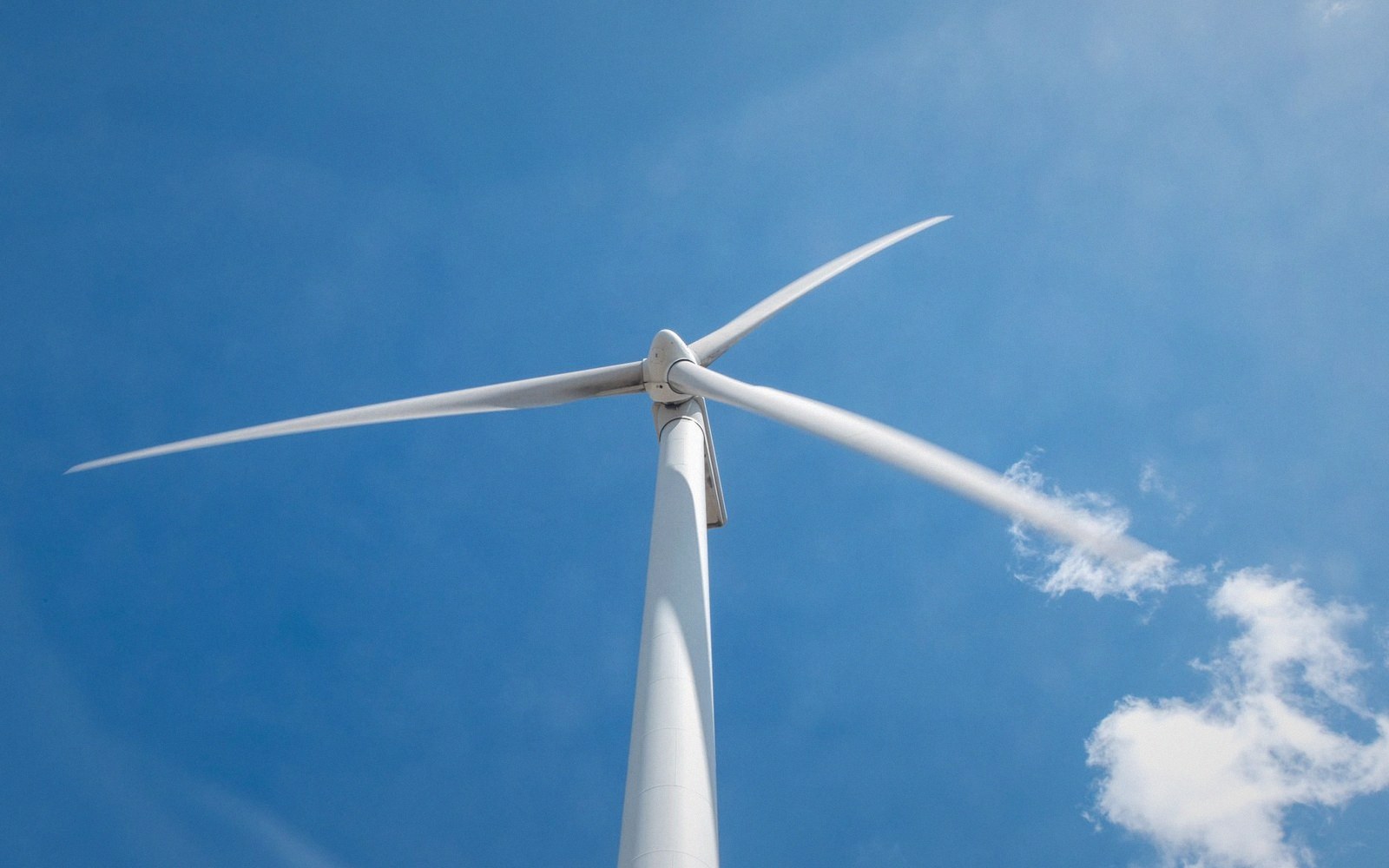 Wind turbine blades spinning against a clear blue sky with wispy clouds