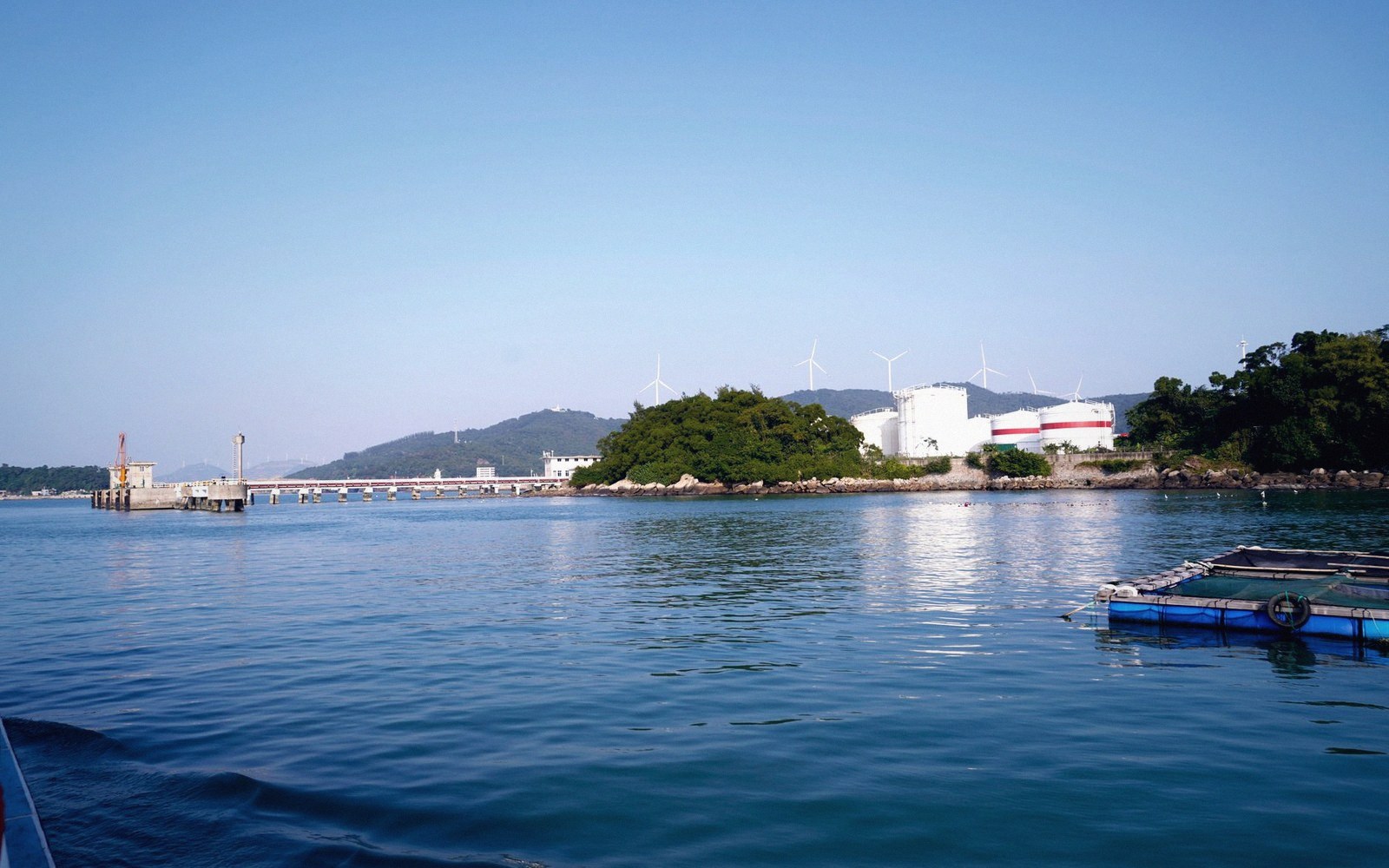 Wind turbines and storage tanks on a coastal island seen across calm water