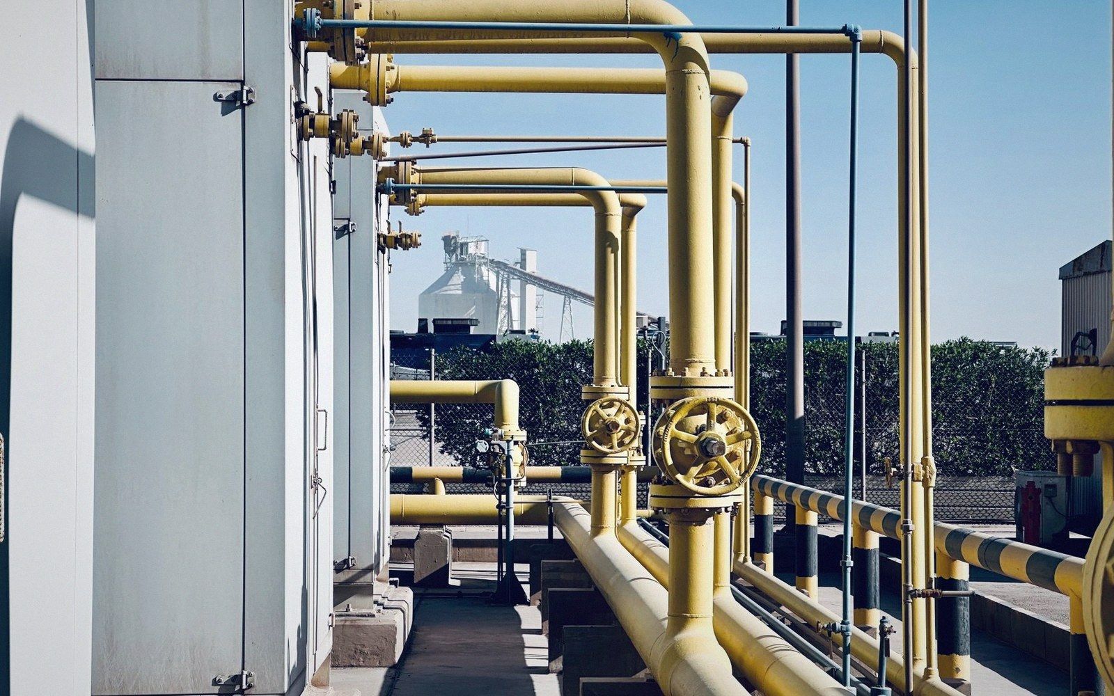 Yellow industrial pipes with valve wheels line a rooftop at a processing facility