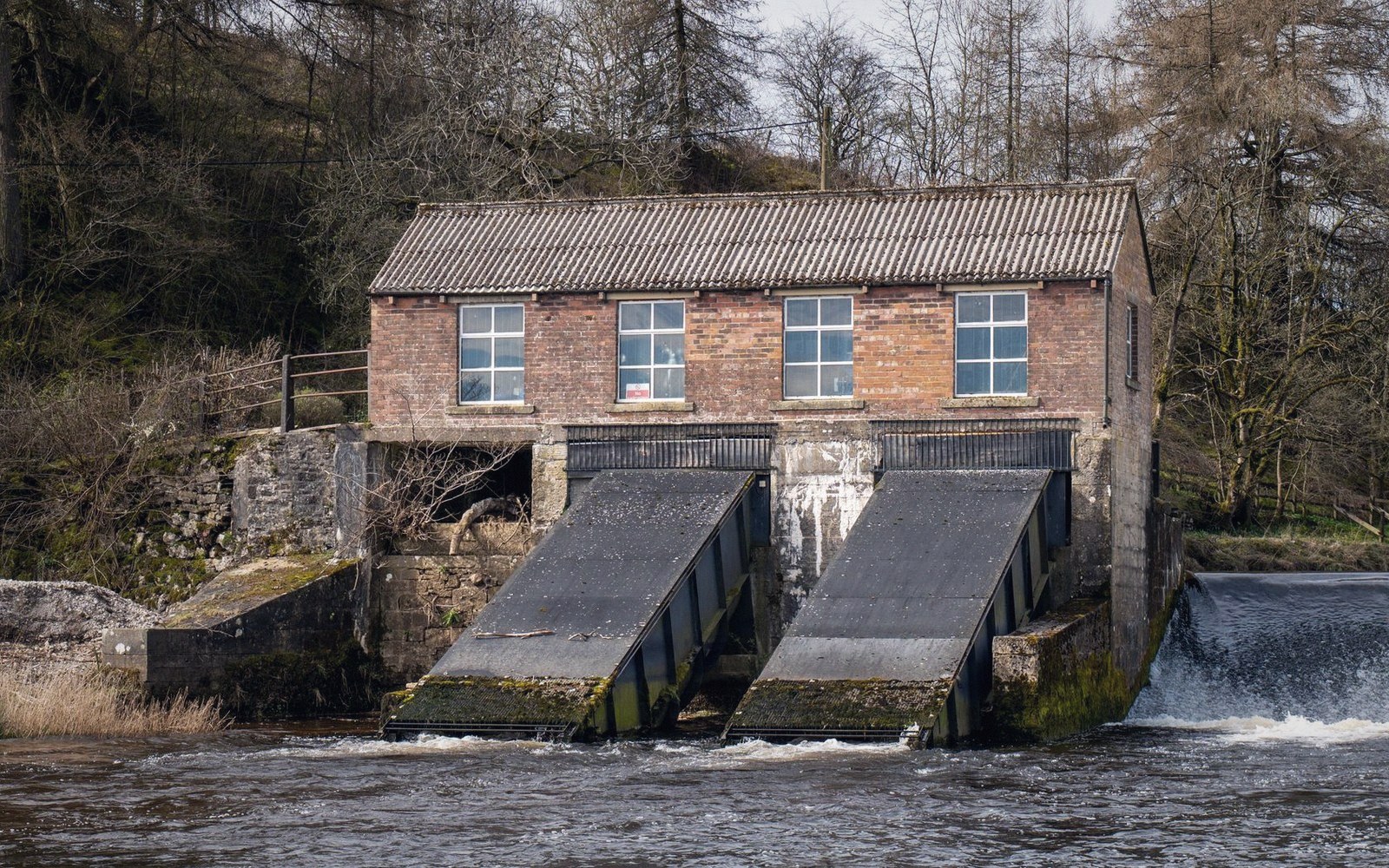 Brick building with two sloped water intake screens above a river weir