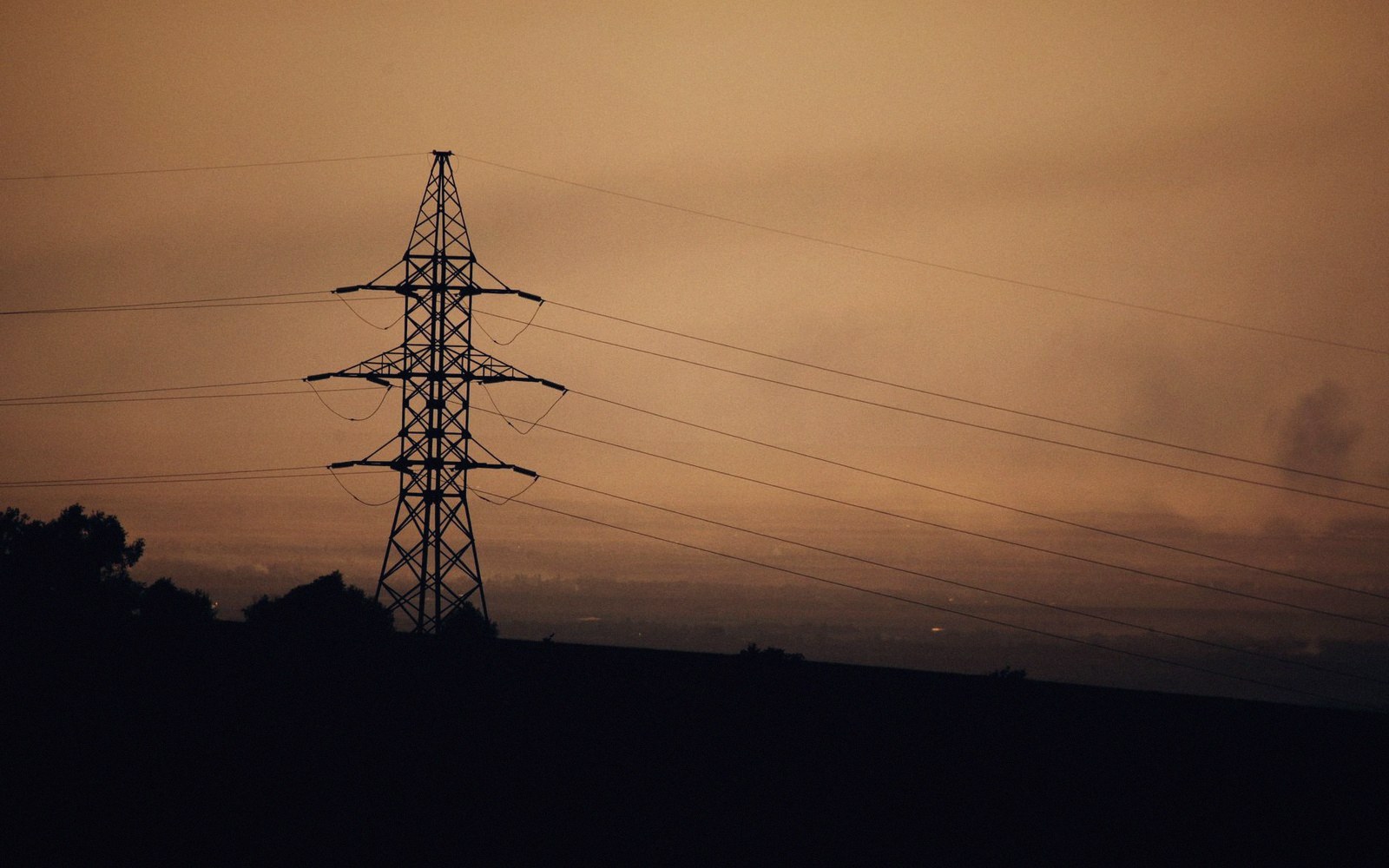 Silhouette of an electricity transmission tower and power lines against a hazy dusk sky