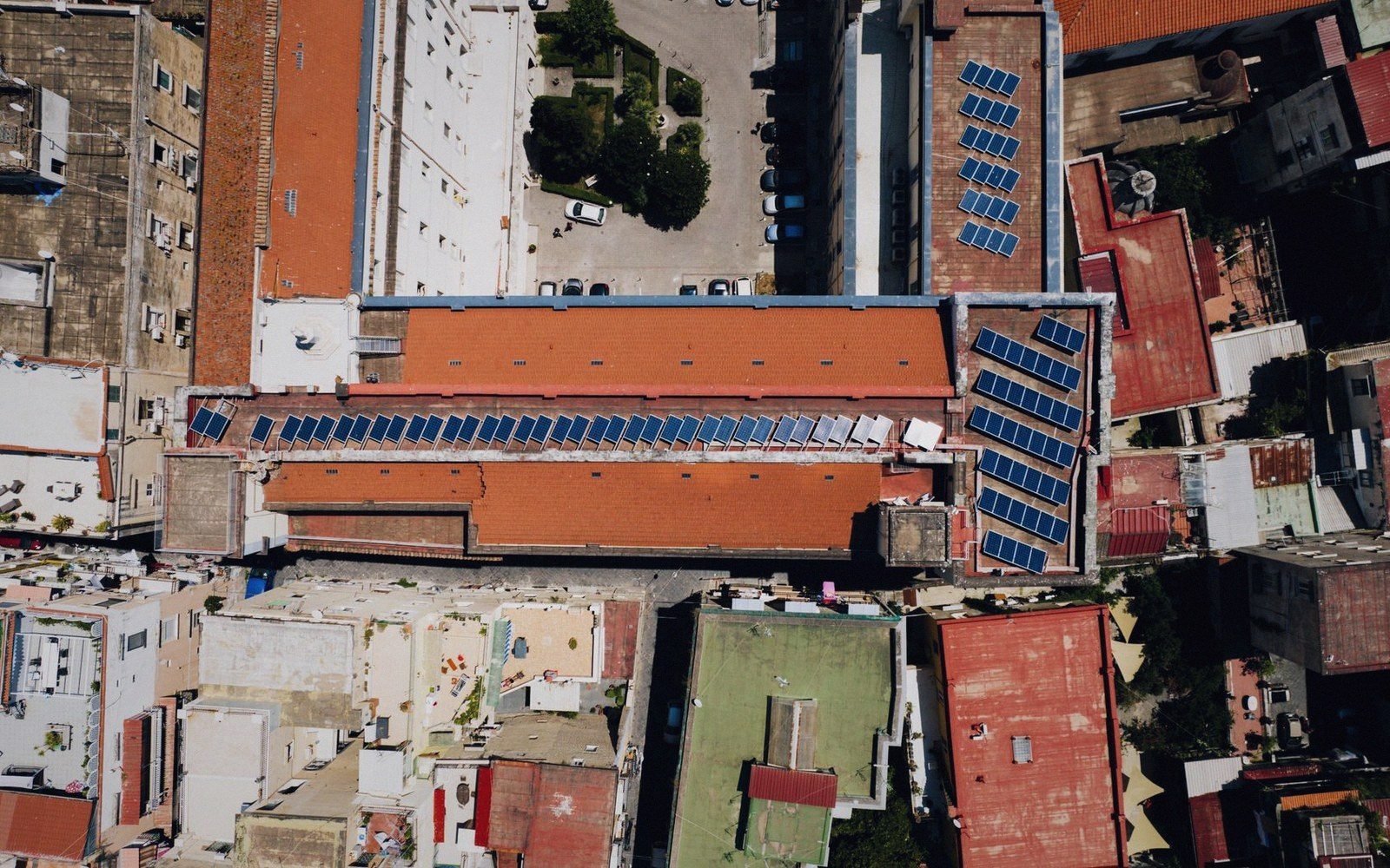 Aerial view of solar panels covering rooftops amid dense urban buildings with terracotta roofs