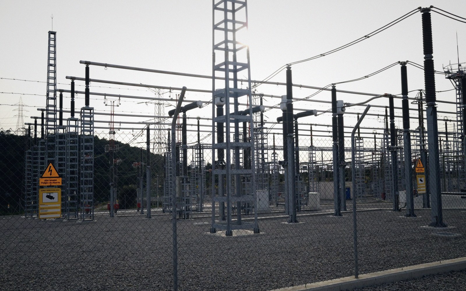 A high-voltage switchyard in flat daylight, steel lattice and porcelain insulators